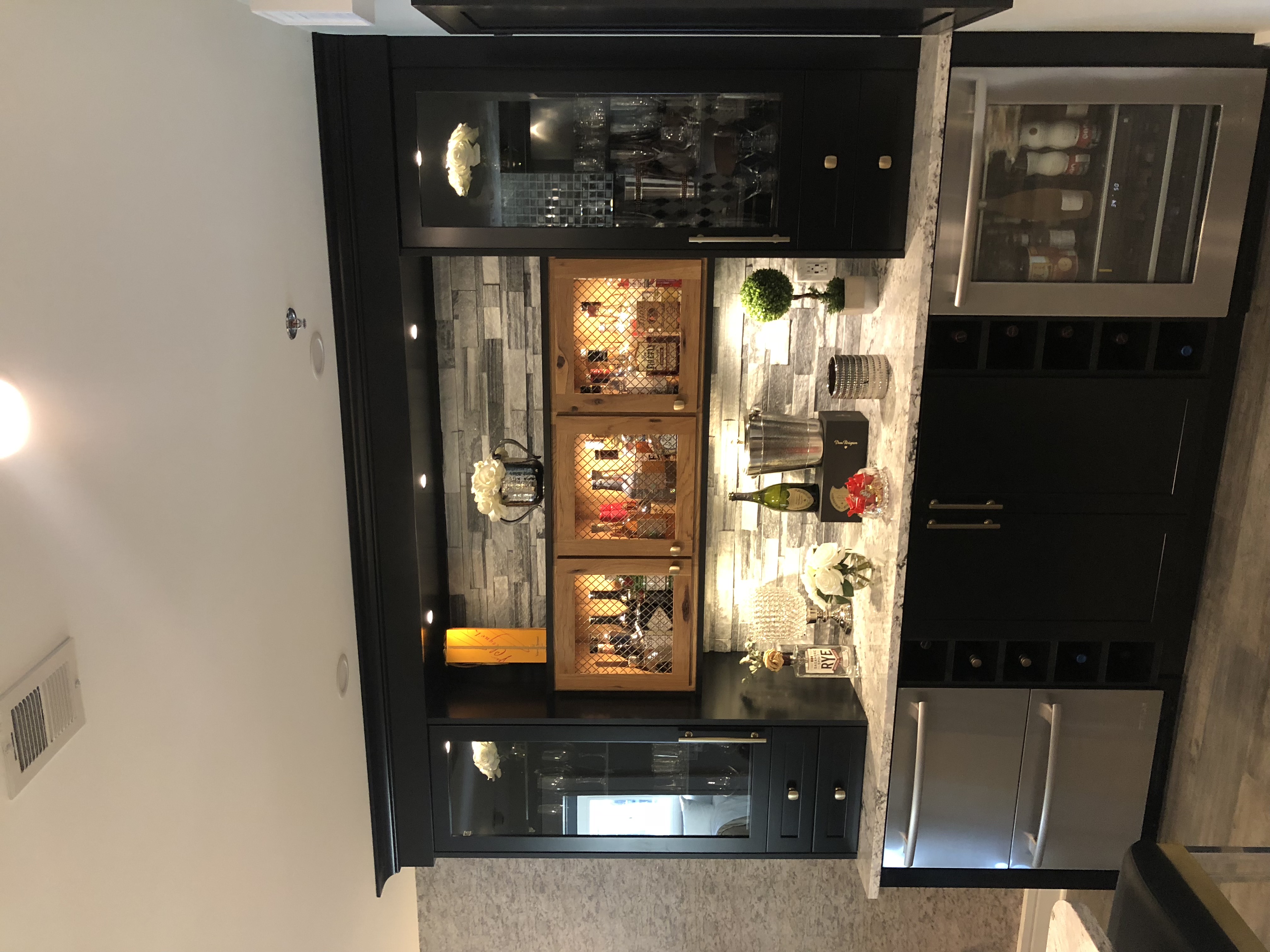 A counter-top bar, with glassware in cabinets on either side and stainless steel appliances with wine and storage underneath