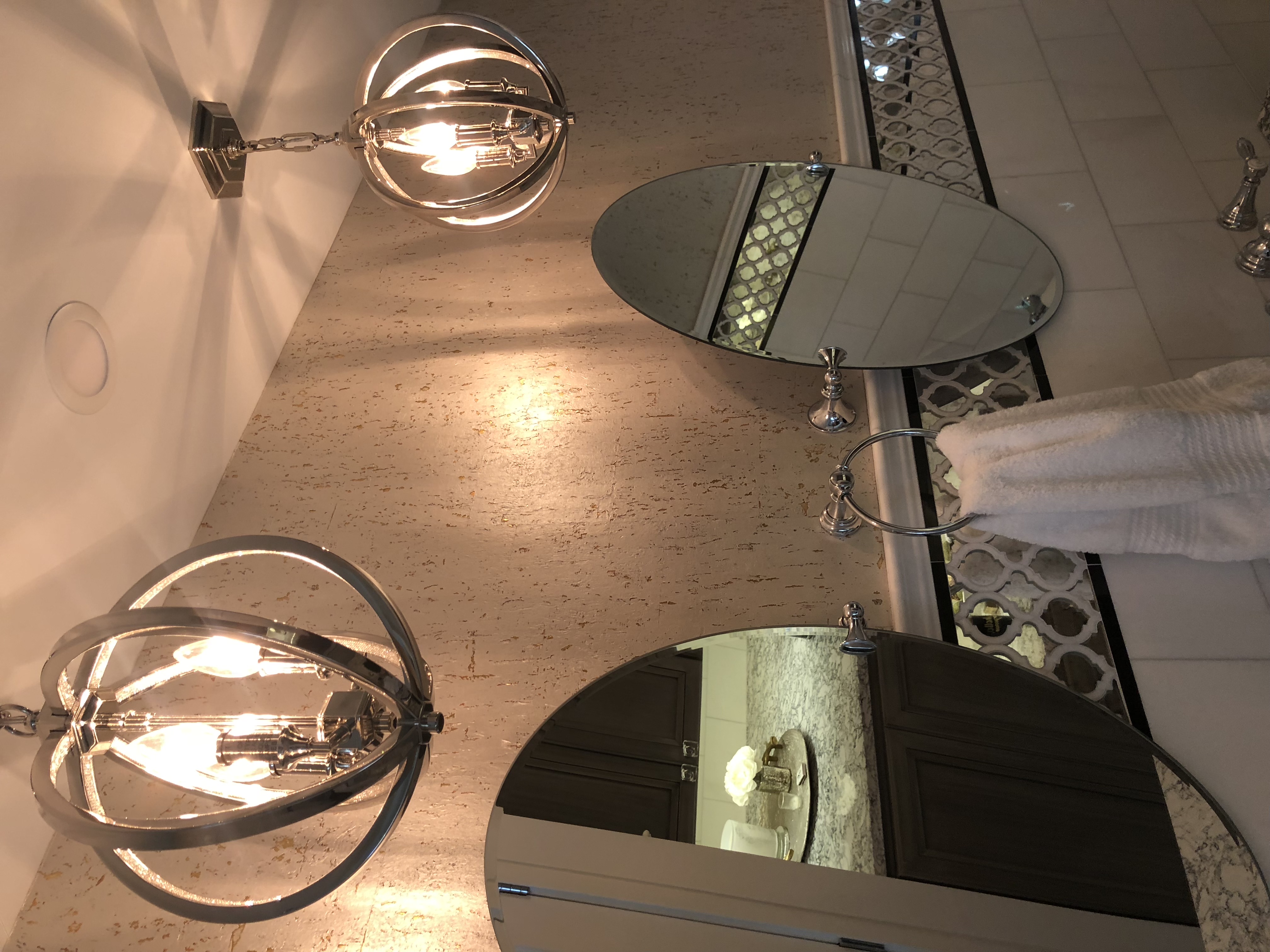 A close up of the oval mirrors and chandeliers above the dual sinks